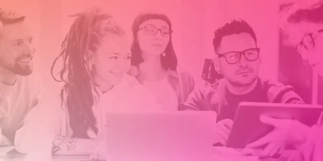 Image shows a group of people gathered around a desk. One person is holding an iPad and showing what's on it to the group.